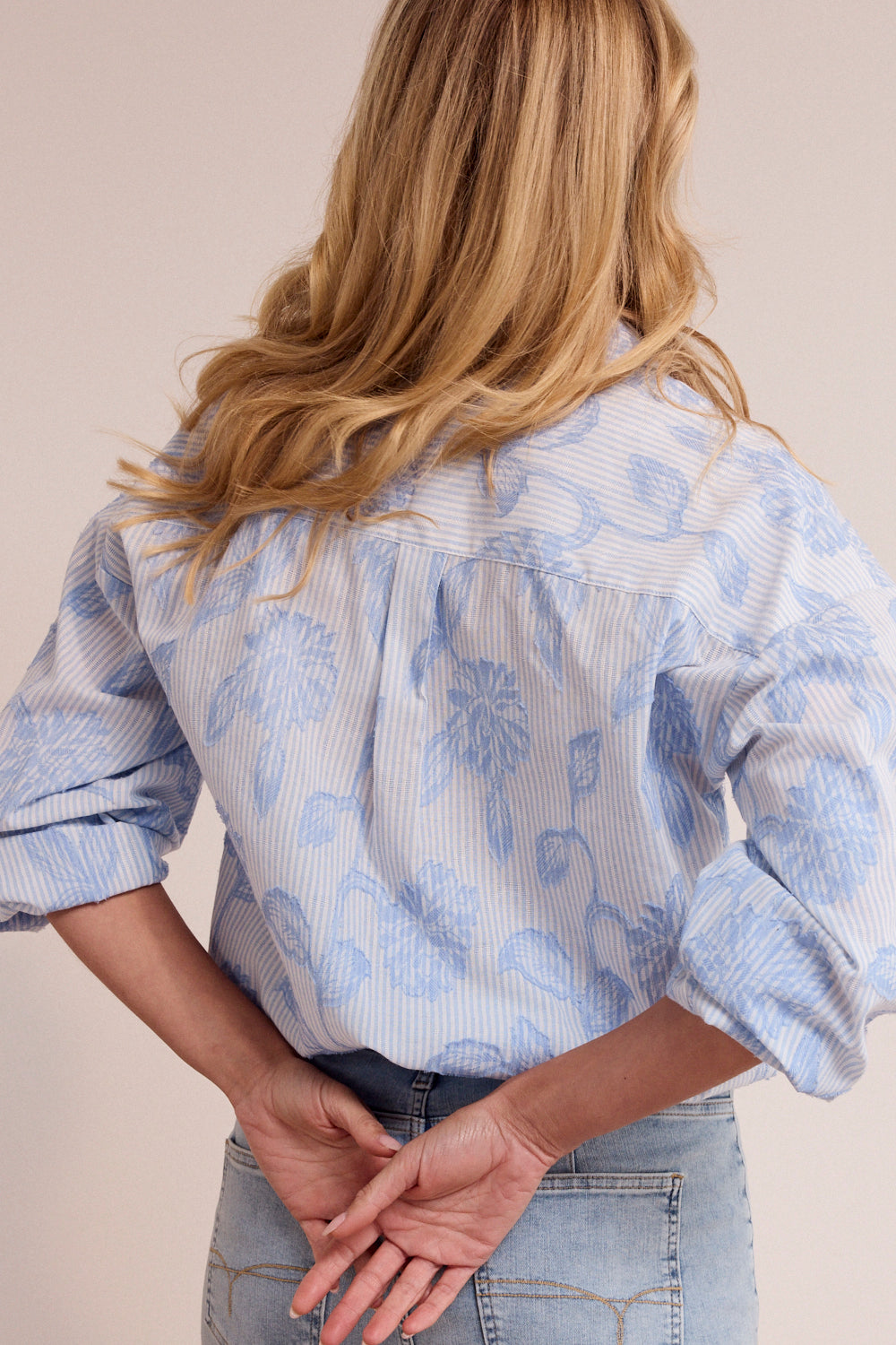Person wearing a light blue floral blouse with rolled-up sleeves on a plain background