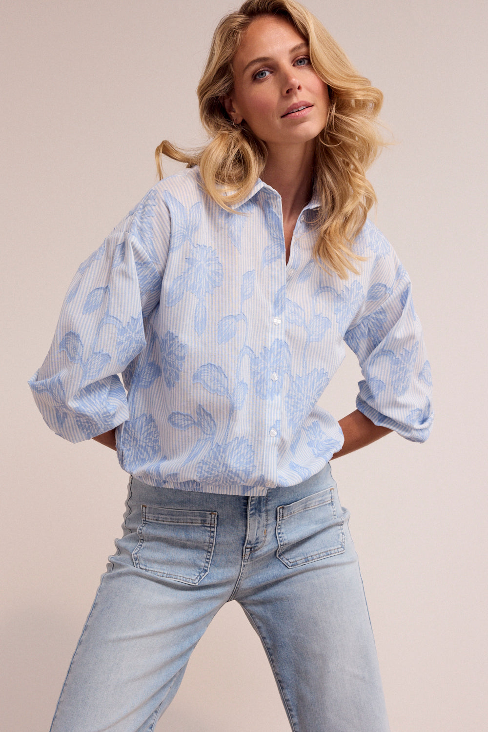 Woman wearing a light blue floral blouse and jeans against a plain background