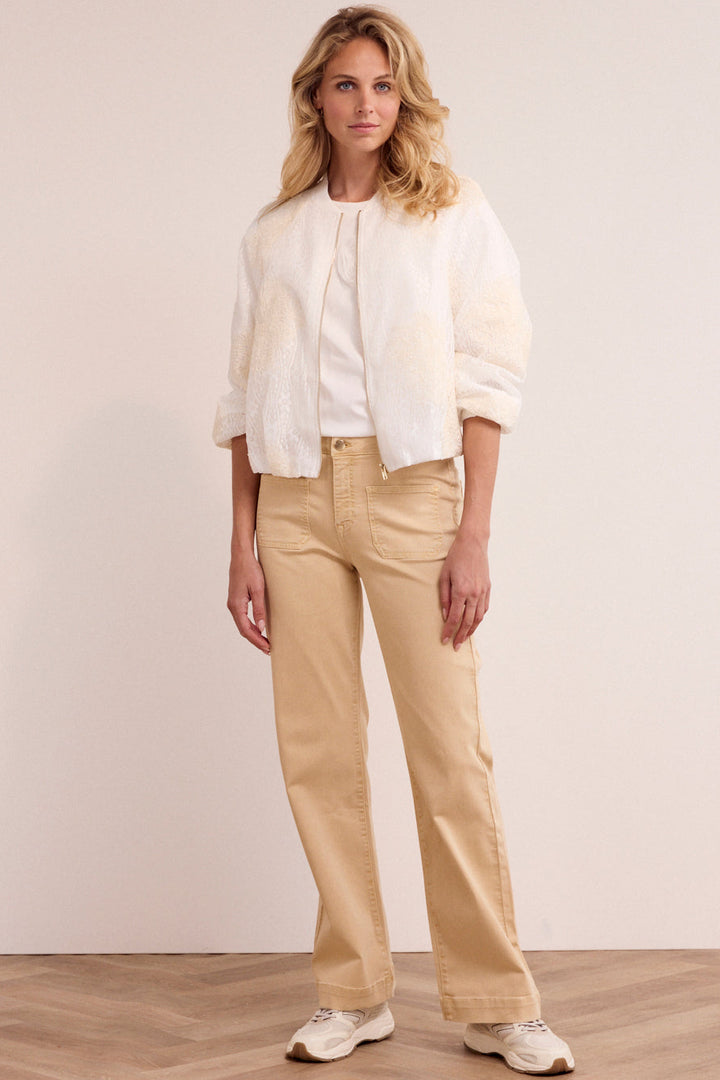 Woman wearing a white blouse and beige pants against a plain background