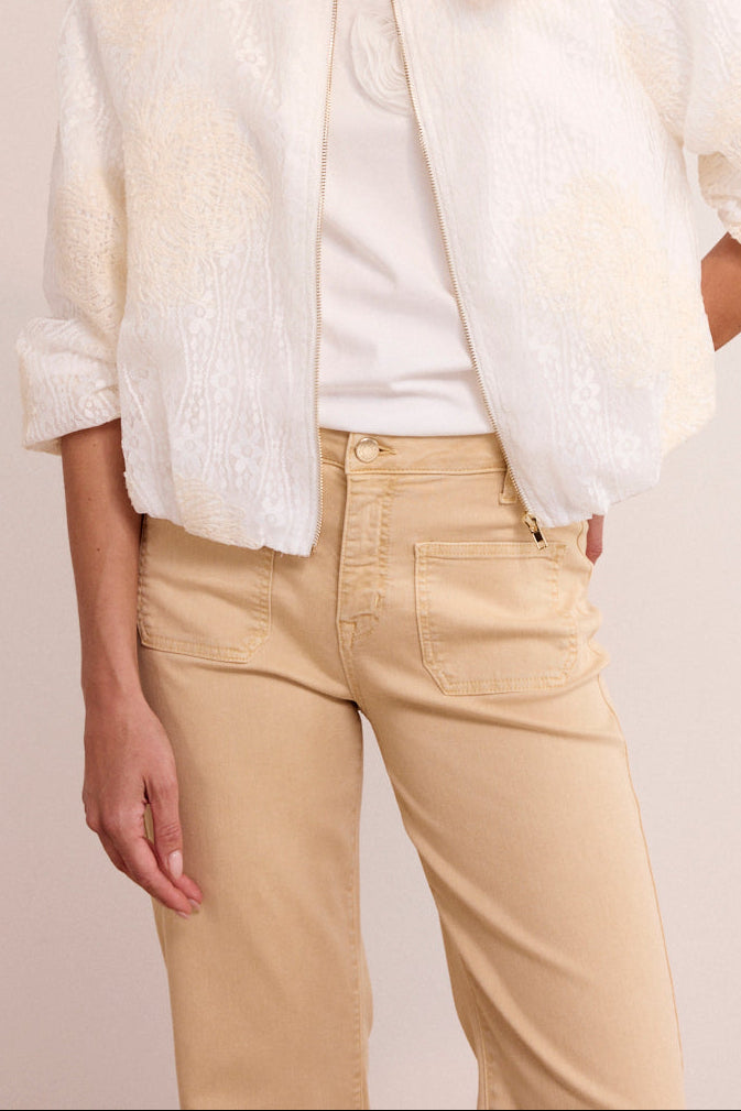 Woman wearing a white jacket, white shirt, and beige pants on a plain background