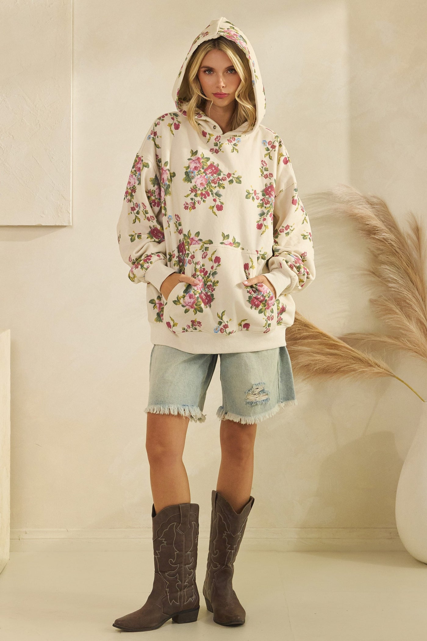 Woman wearing a floral hoodie and denim shorts with cowboy boots indoors.