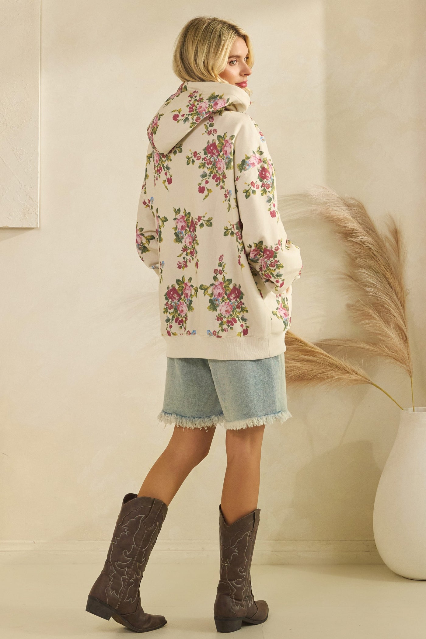 Woman wearing a floral coat and denim skirt with brown boots in a minimalistic setting.