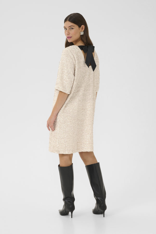 Woman wearing a beige dress with a black bow and black knee-high boots on a white background