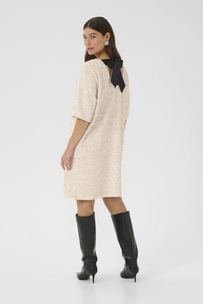 Woman wearing a beige dress with a black bow and black knee-high boots on a white background