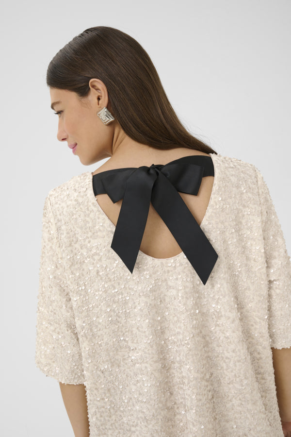 Woman wearing a beige top with a black bow at the back against a white background