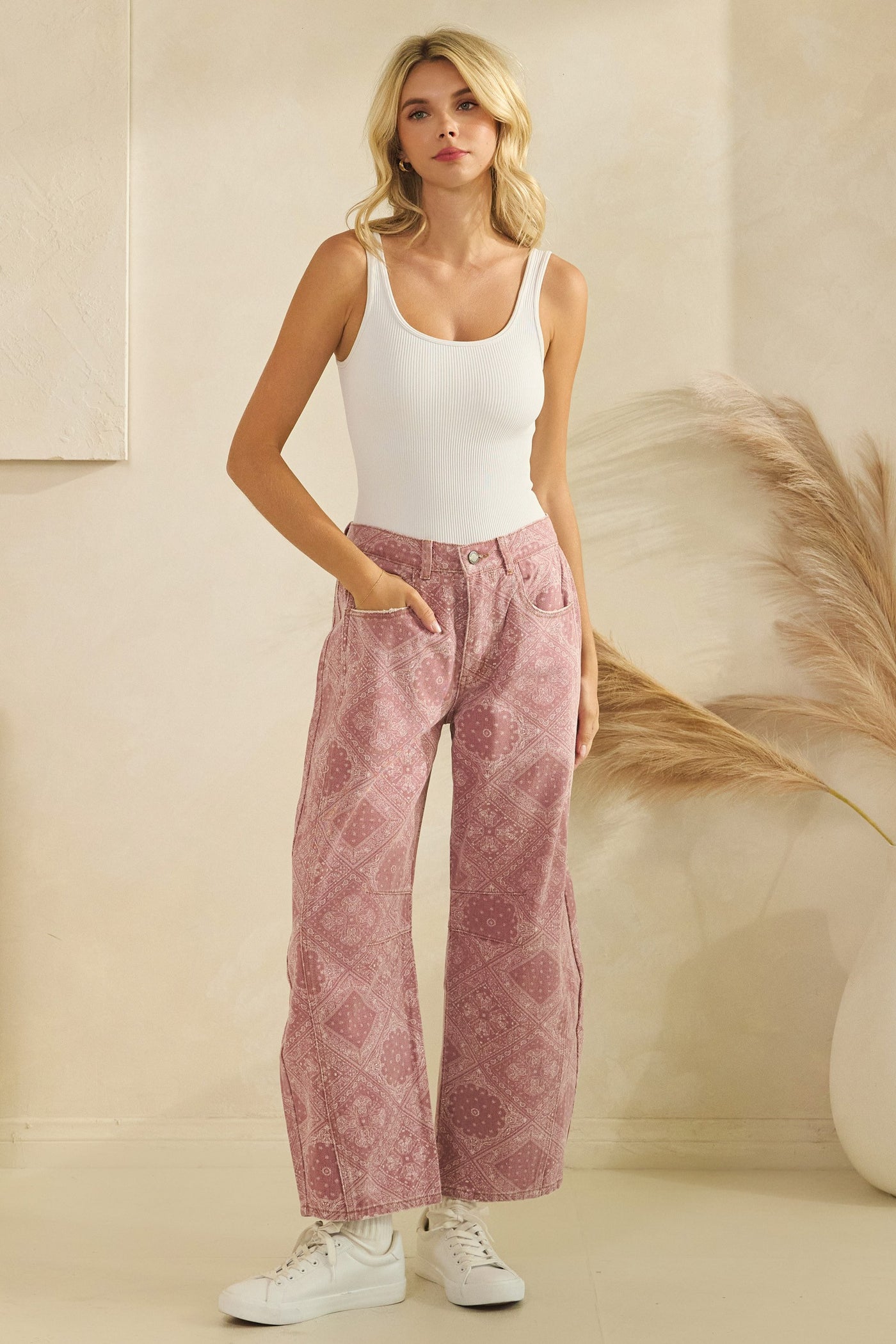 Woman wearing a white tank top and pink patterned pants against a neutral background