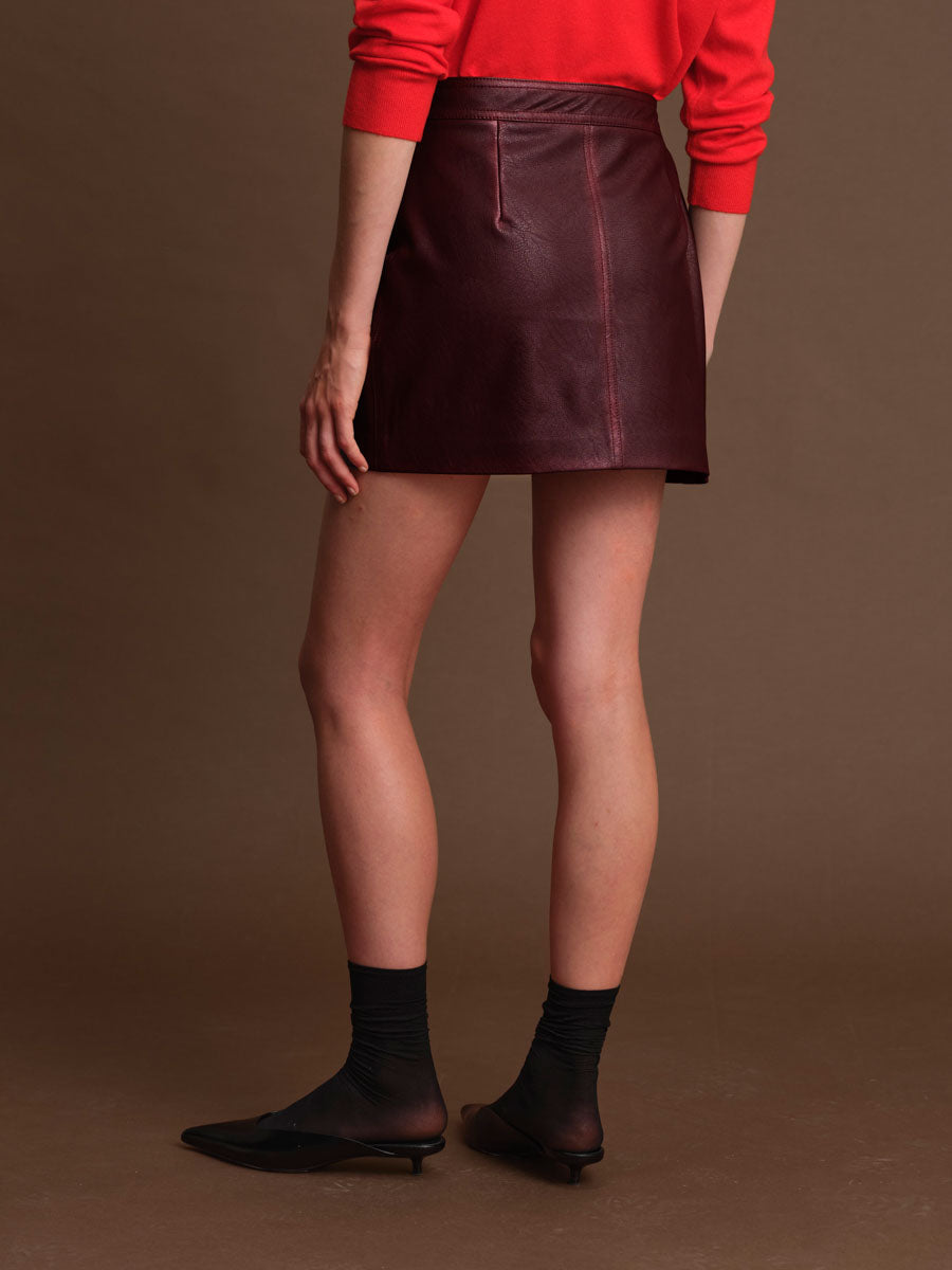 Person wearing a red sweater and brown leather skirt on a brown background