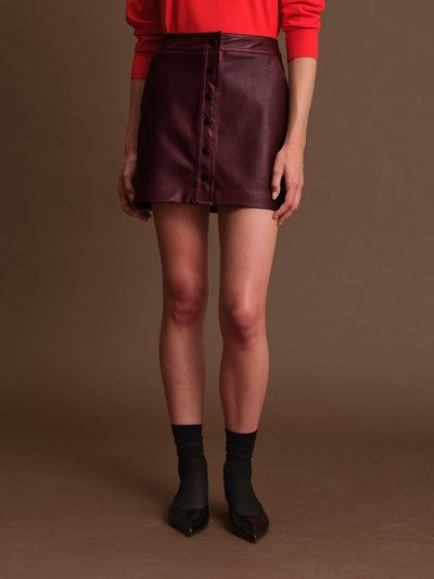 Person wearing a red top and maroon leather skirt on a brown background