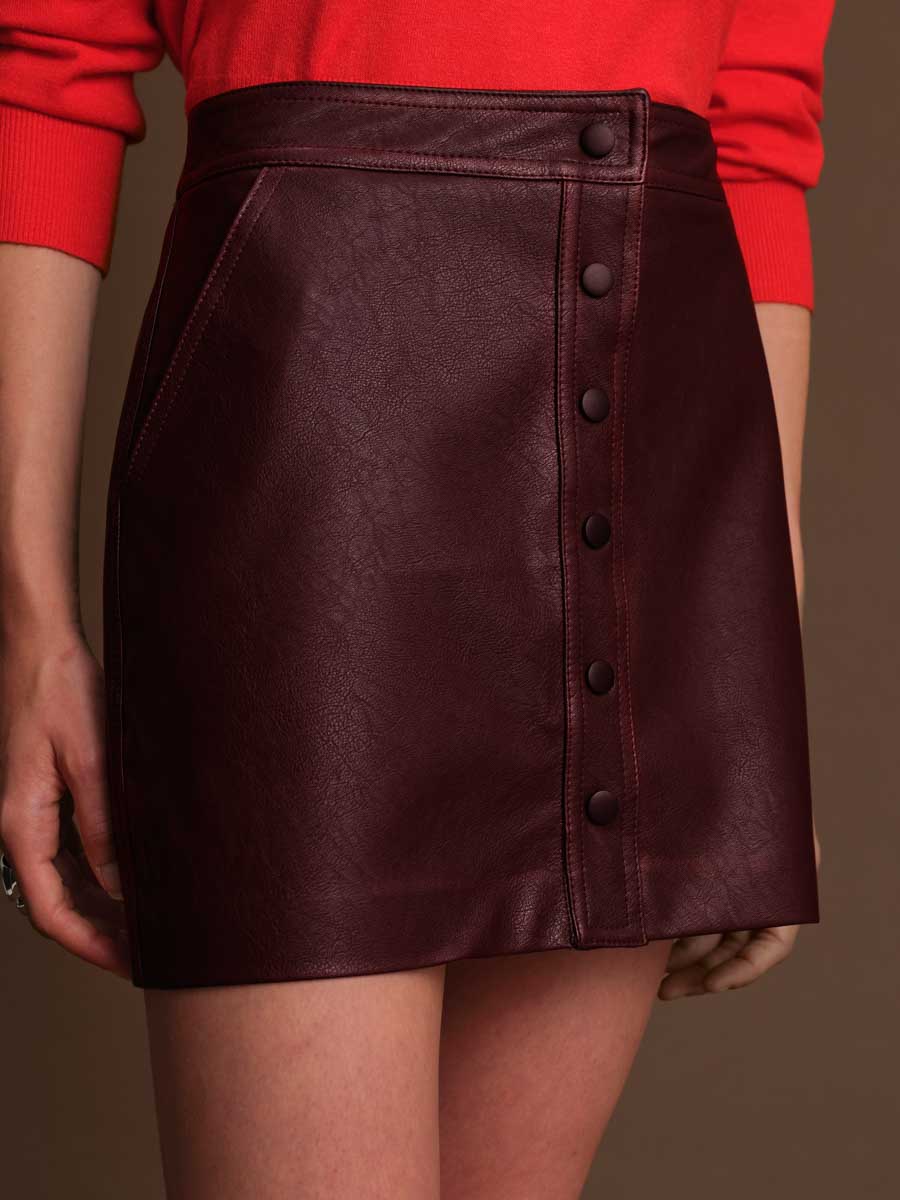 Brown leather skirt with button details worn by a person in a red top on a brown background