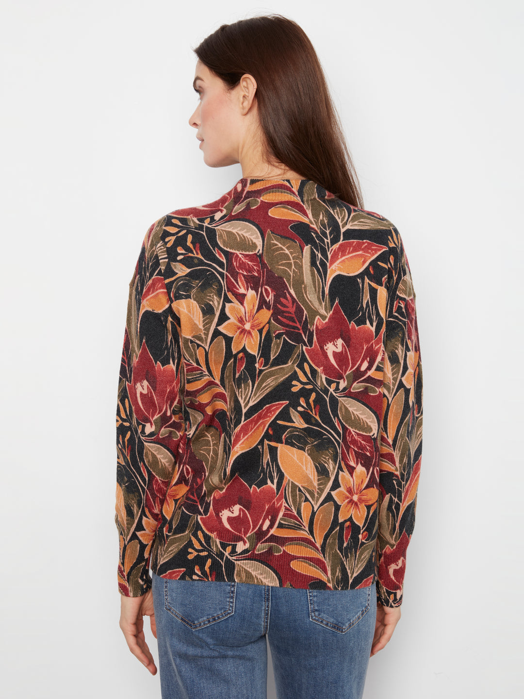 A woman shown from the back wearing a long-sleeve blouse with an intricate botanical floral pattern in red, orange, and brown tones, paired with blue jeans against a plain white background.