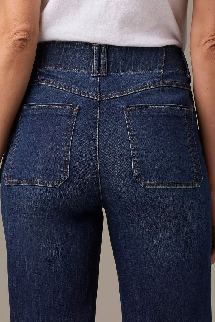Close-up back view of a person wearing dark blue denim jeans with a white top, showing the back pockets and waistband.