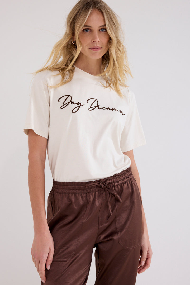 A woman wearing a cream-colored short-sleeve t-shirt with &