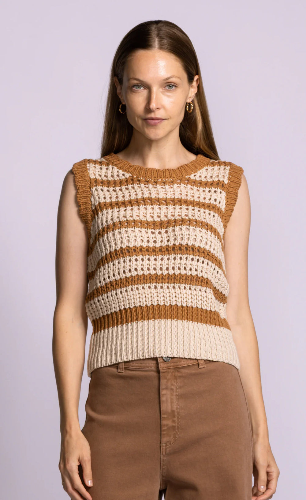 Woman wearing a sleeveless crochet top with brown and beige stripes on a light purple background