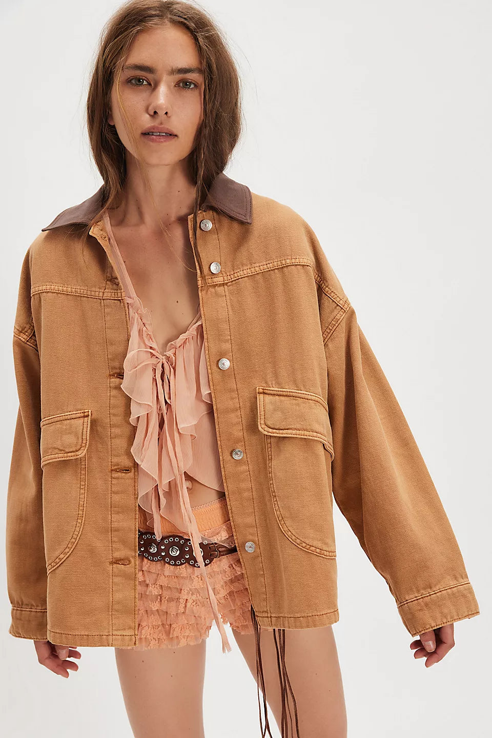 Woman wearing a tan jacket over a sheer top and skirt on a white background