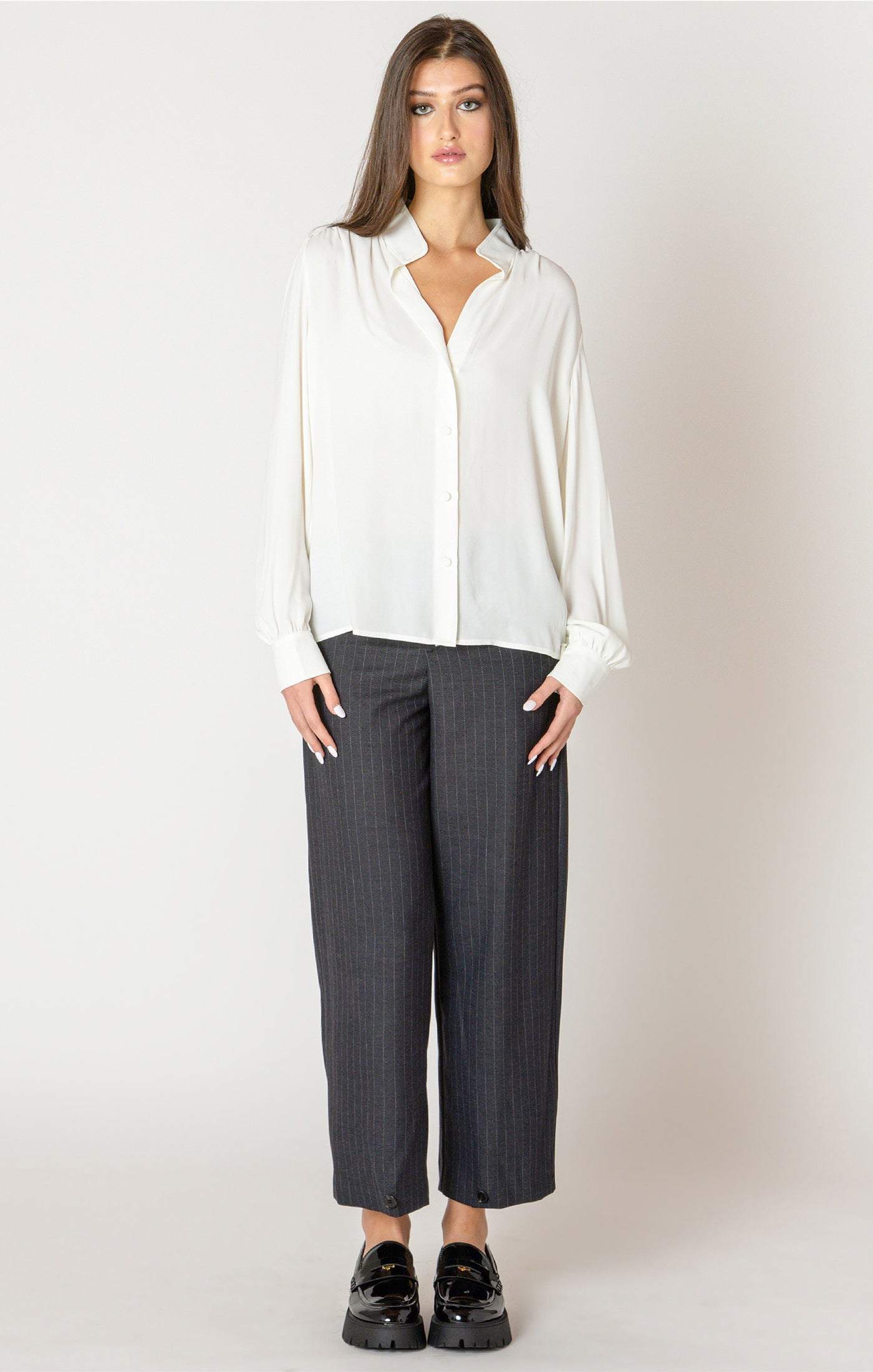 Woman wearing a white blouse and gray pants against a plain background