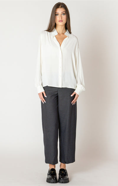 Woman wearing a white blouse and gray pants against a plain background