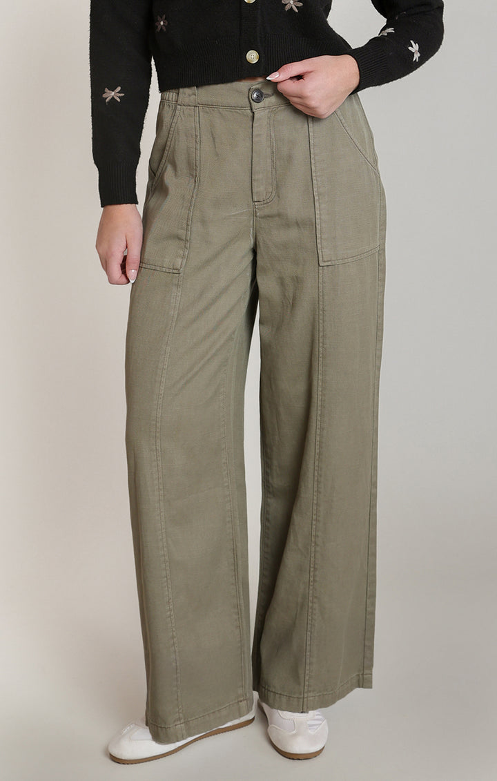 A person wearing high-waisted, wide-leg utility pants in a muted olive green color, styled with a black embroidered long-sleeve top and white sneakers against a plain light gray studio background.