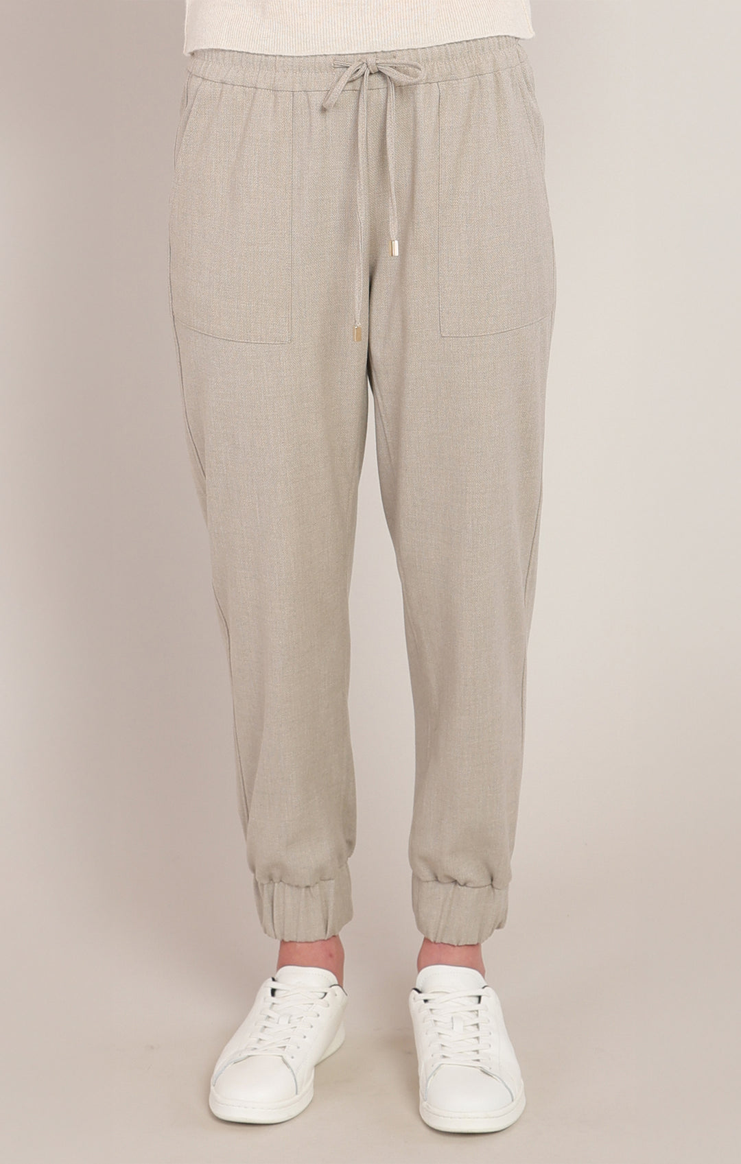 Beige jogger pants worn with white sneakers on a beige background