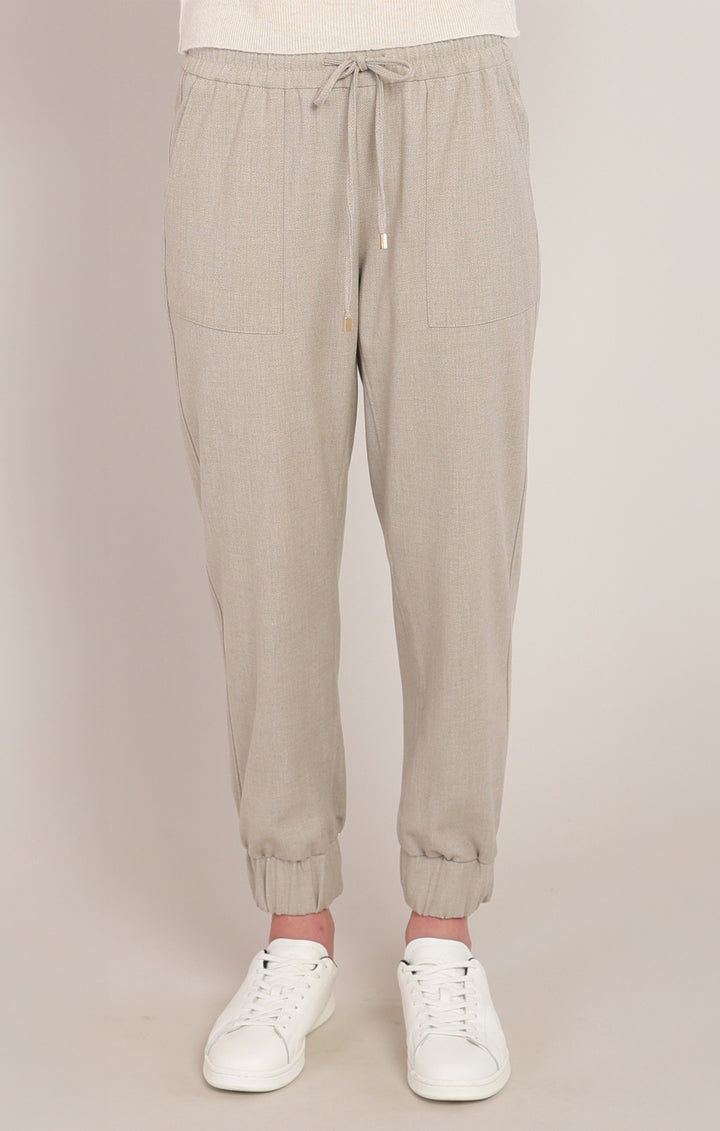 Beige jogger pants worn with white sneakers on a beige background