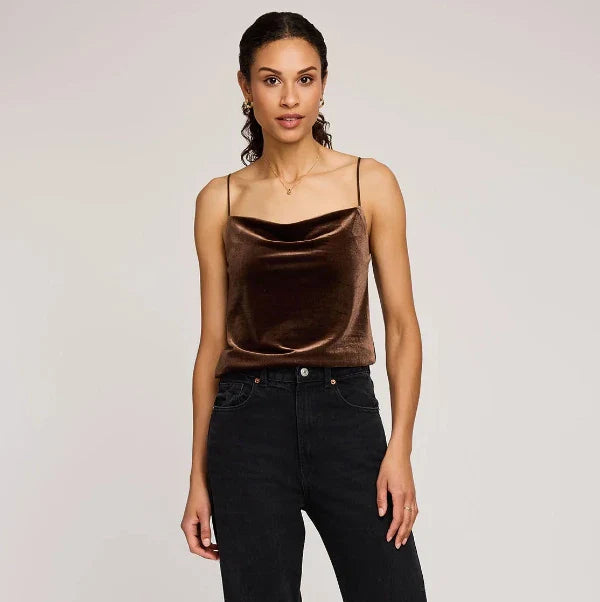 Woman wearing a brown satin camisole and black jeans against a plain background