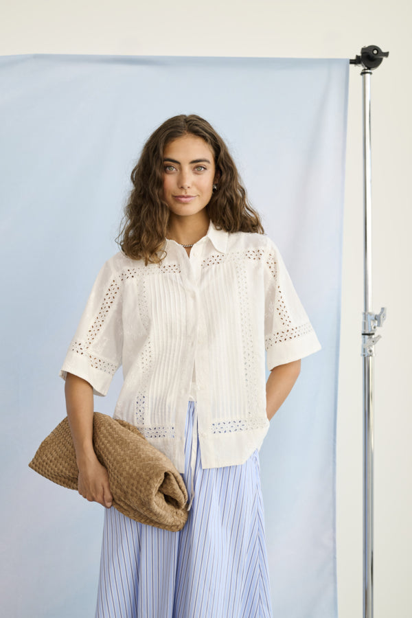 Woman wearing a white blouse with intricate patterns against a light blue background