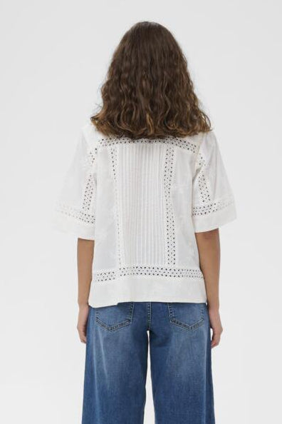 Person wearing a white embroidered top and blue jeans on a white background
