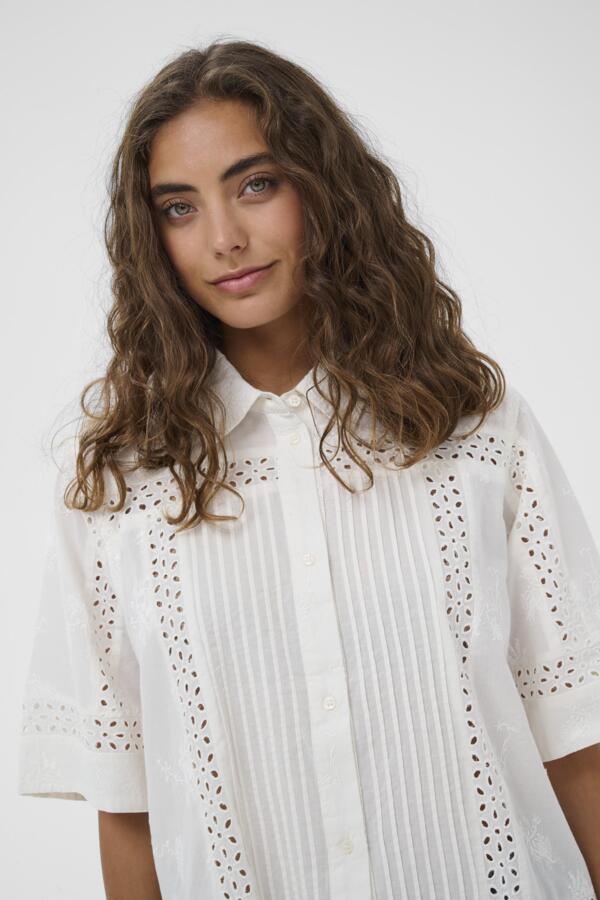 Woman wearing a white blouse with intricate patterns on a plain background