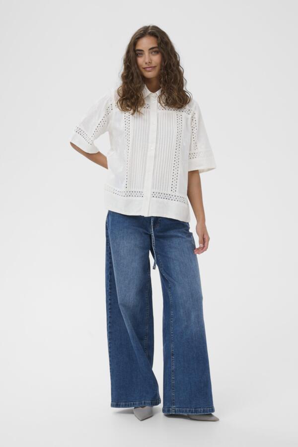 Woman wearing a white blouse with lace details and blue jeans on a white background