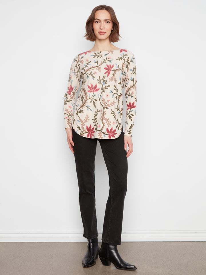 Woman wearing a floral blouse and black pants against a white background