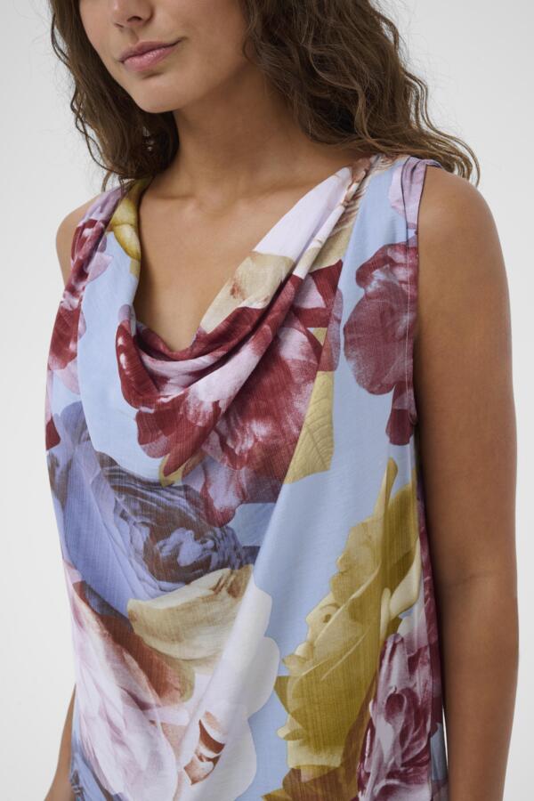 Woman wearing a sleeveless top with a floral and landscape print on a white background