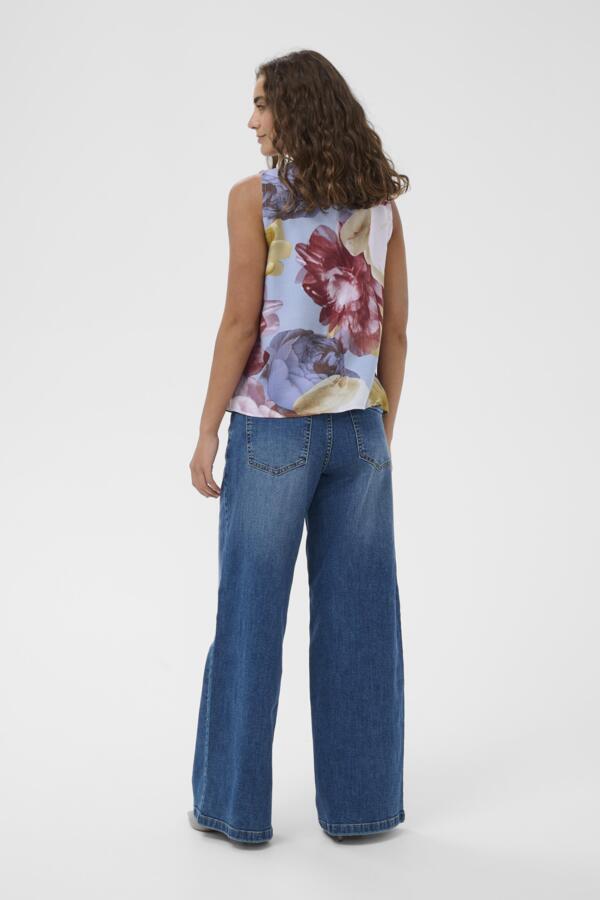 Woman wearing a floral sleeveless top and blue jeans on a white background