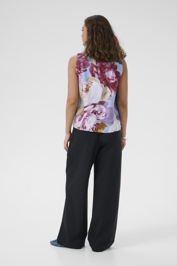 Woman wearing a floral sleeveless top and black pants on a white background