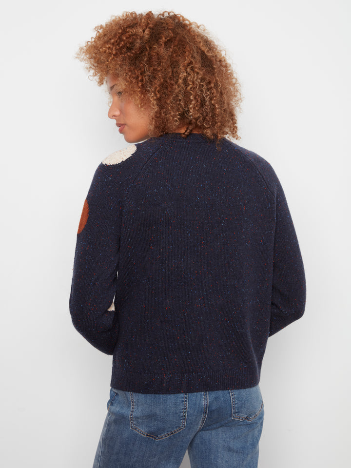 A person shown from the back wearing a dark navy knit sweater with a white textured yoke and a brown patch on the upper sleeve, paired with blue jeans against a plain light background.