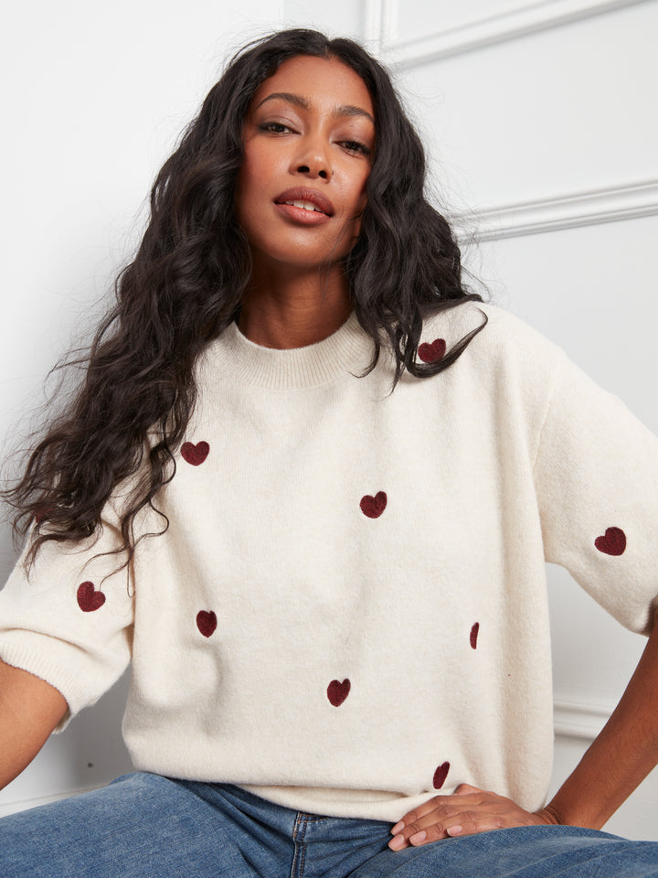 Woman wearing a cream sweater with red heart patterns against a white background