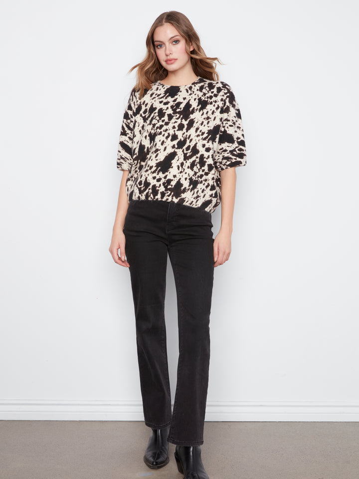 Woman wearing a patterned top and black pants against a white background