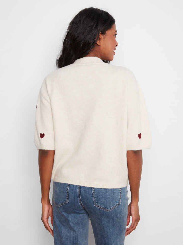 Person wearing a cream-colored shirt with heart details on a white background