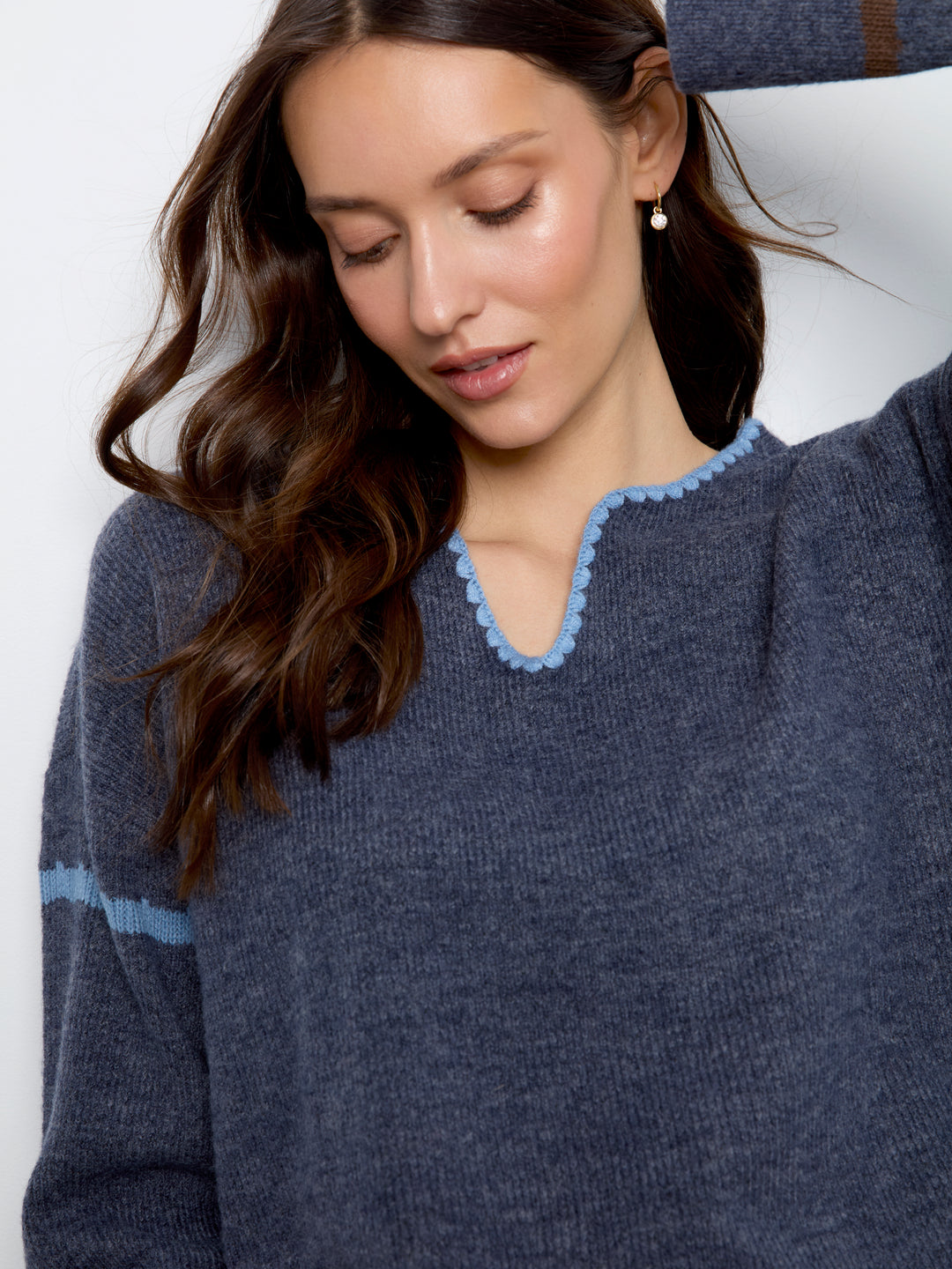 A close-up of a woman wearing a dark slate blue knit sweater with a light blue scalloped trim around the split neckline and a matching light blue stripe on the sleeve.