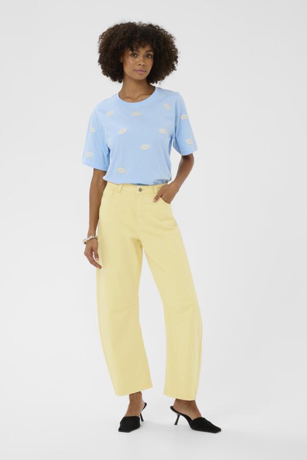 Woman wearing a light blue top with cloud patterns and yellow pants on a white background