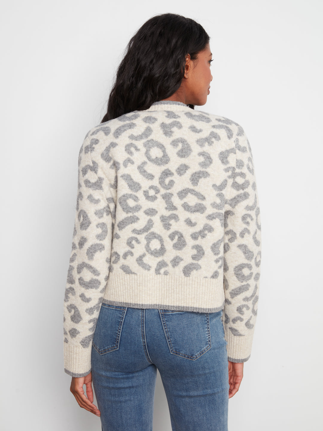 Person wearing a leopard print sweater and blue jeans on a white background