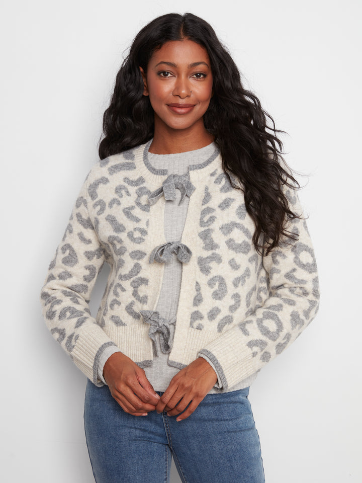 Woman wearing a white sweater with gray leopard print pattern on a plain background