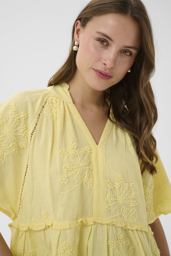 Woman wearing a yellow embroidered dress against a white background