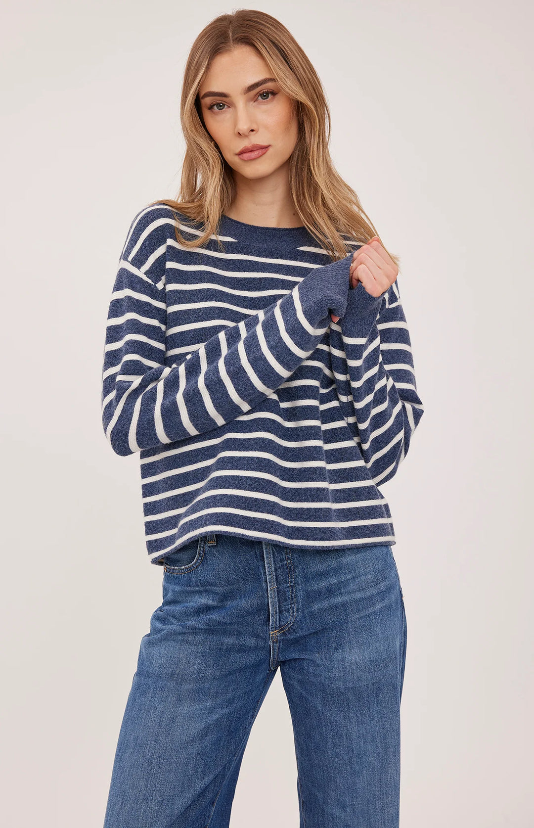 A woman modeling a navy blue and white horizontally striped long-sleeve knit sweater with blue jeans, photographed against a plain light background.