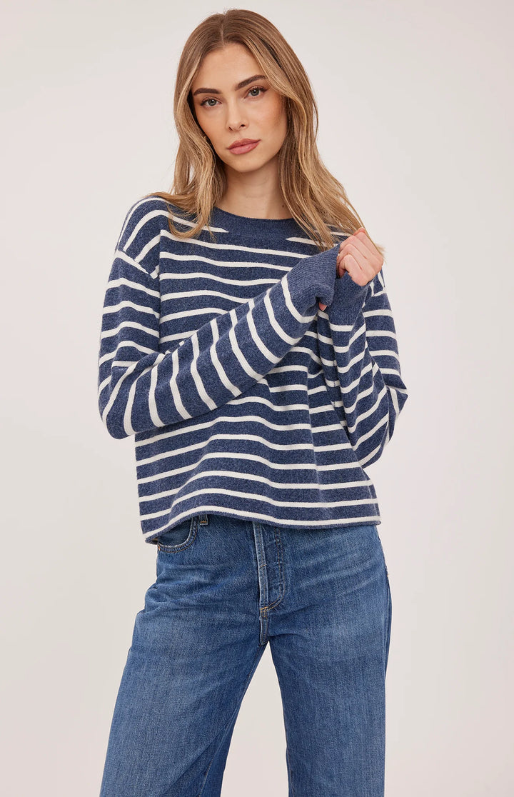 A woman modeling a navy blue and white horizontally striped long-sleeve knit sweater with blue jeans, photographed against a plain light background.