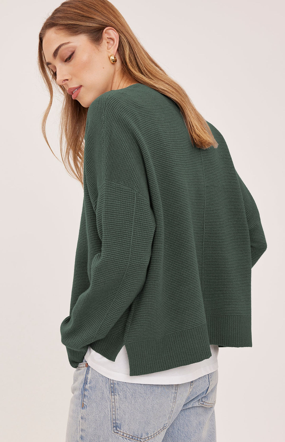 A woman wearing a dark green ribbed knit sweater, shown from a side-back angle against a plain light background.