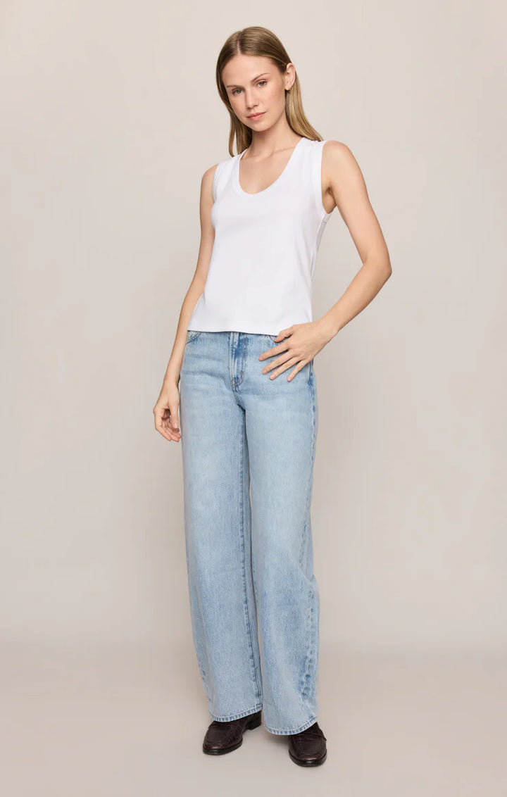 Woman wearing a white tank top and light blue jeans on a plain background