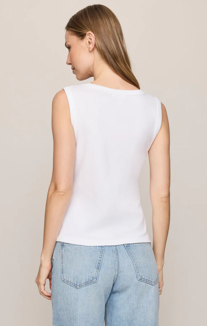 Woman wearing a white sleeveless top and light blue jeans on a beige background