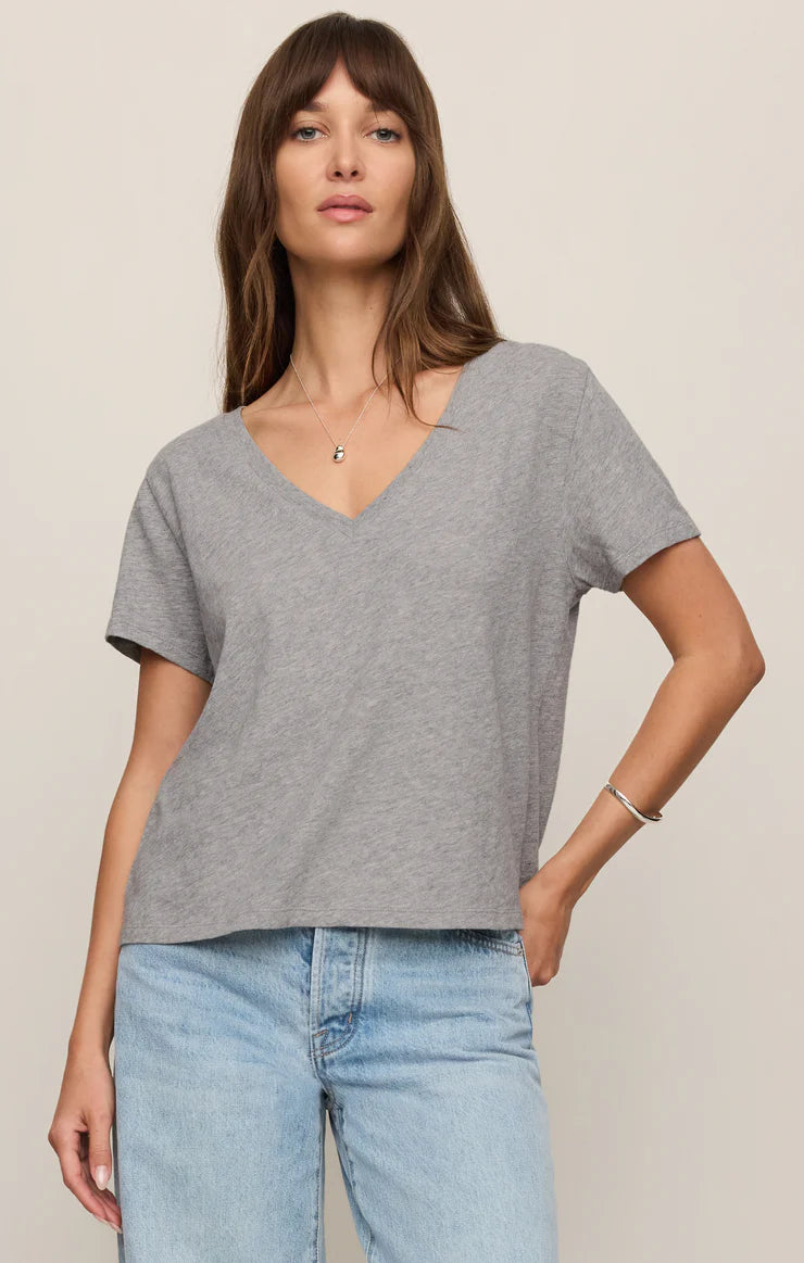 Woman wearing a gray t-shirt and blue jeans against a beige background