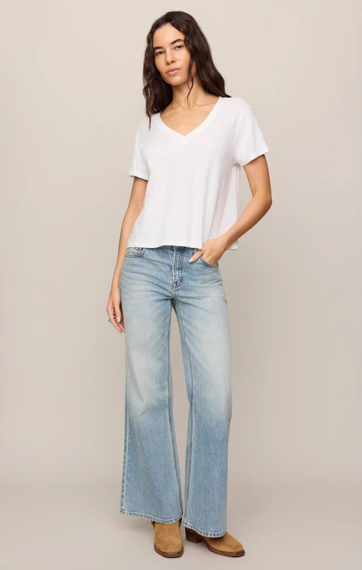 Woman wearing a white t-shirt and blue jeans against a plain background