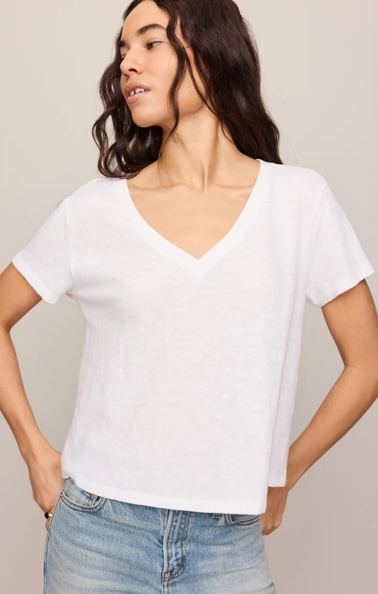 Woman wearing a white V-neck t-shirt and blue jeans against a beige background
