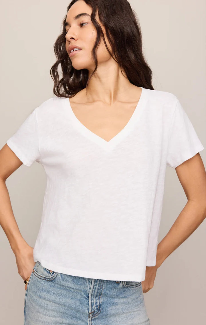 Woman wearing a white V-neck t-shirt and blue jeans against a beige background